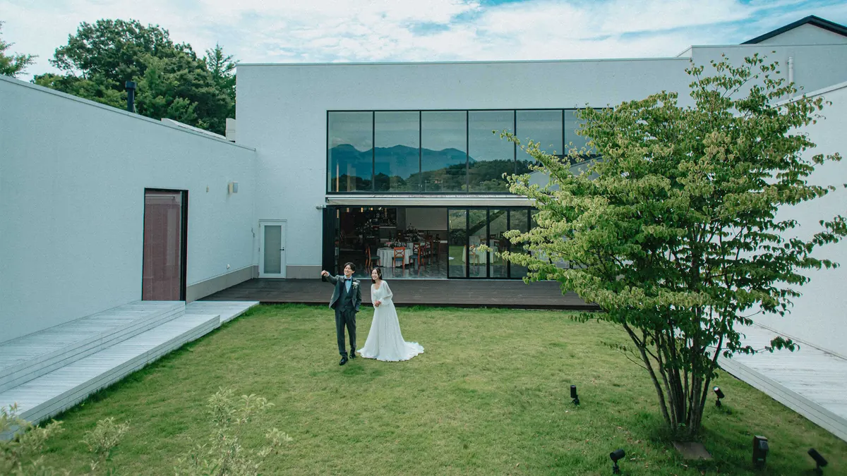 緑の芝生と白い邸宅の前に立つ新郎新婦